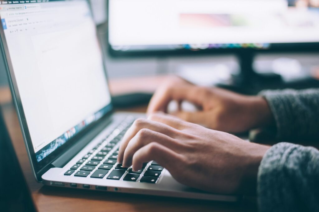 Hände tippen auf einer Laptop-Tastatur auf einem Holzschreibtisch, symbolisch für die professionelle Website-Wartung.